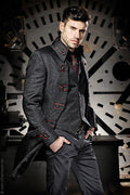 A man wearing a dark patterned double-breasted coat with red button accents, a matching dark vest, and dark trousers, posed in front of a large industrial circular metal structure.