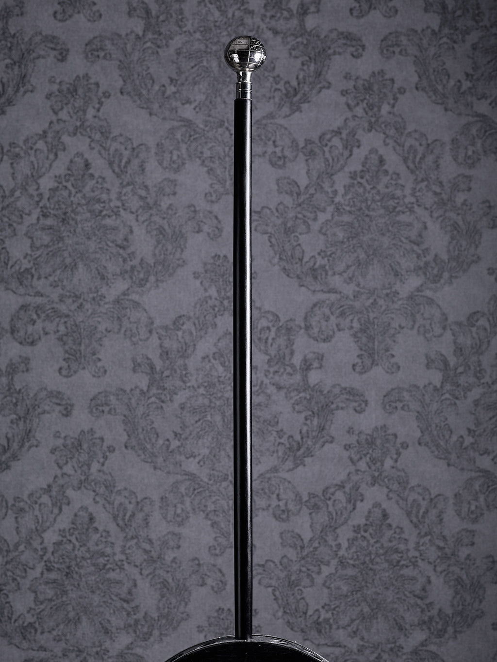 Full-length view of the Atlas walking cane with a silver globe topper and a sleek black shaft on a patterned background