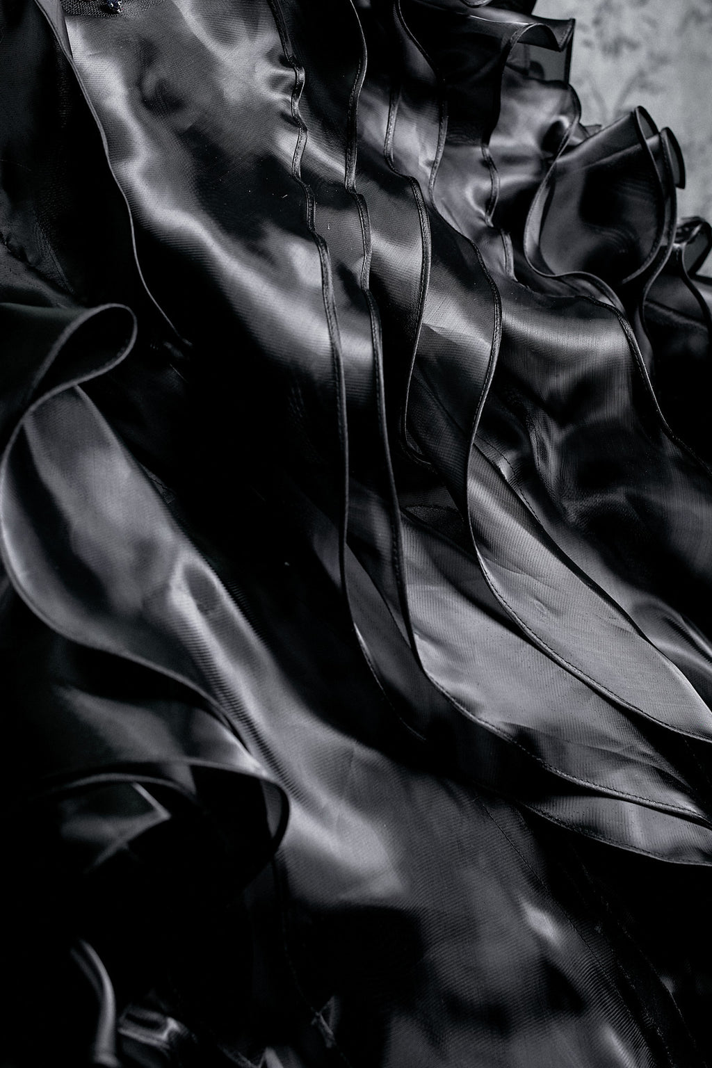 Close-up of voluminous black organza tiered ruffle layers with ribbon trim detailing on gothic wedding ballgown skirt, showing dramatic fabric movement and luxurious texture