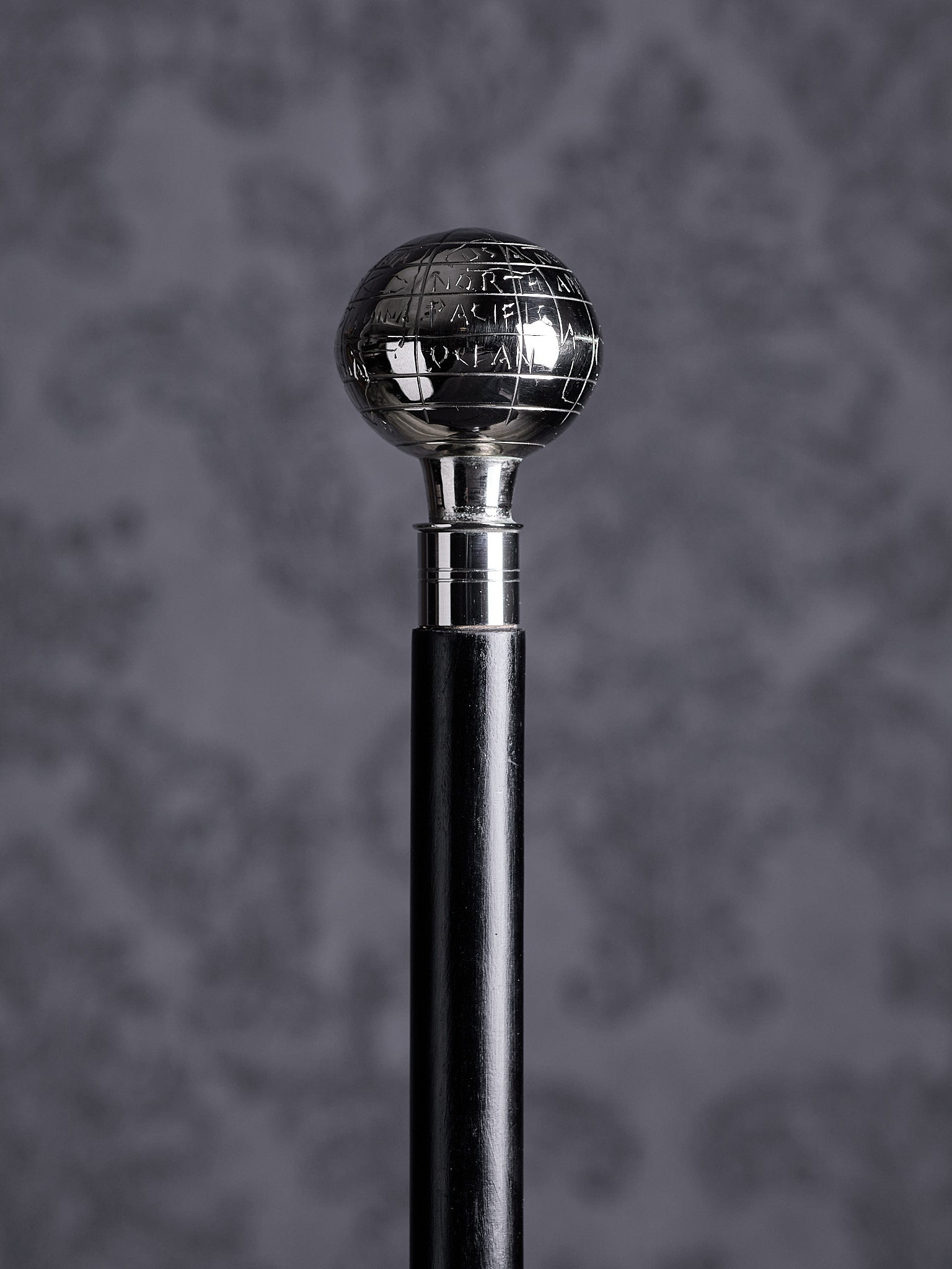 Detailed close-up of the Atlas cane handle, highlighting the engraved names of oceans and geographical lines on the silver sphere