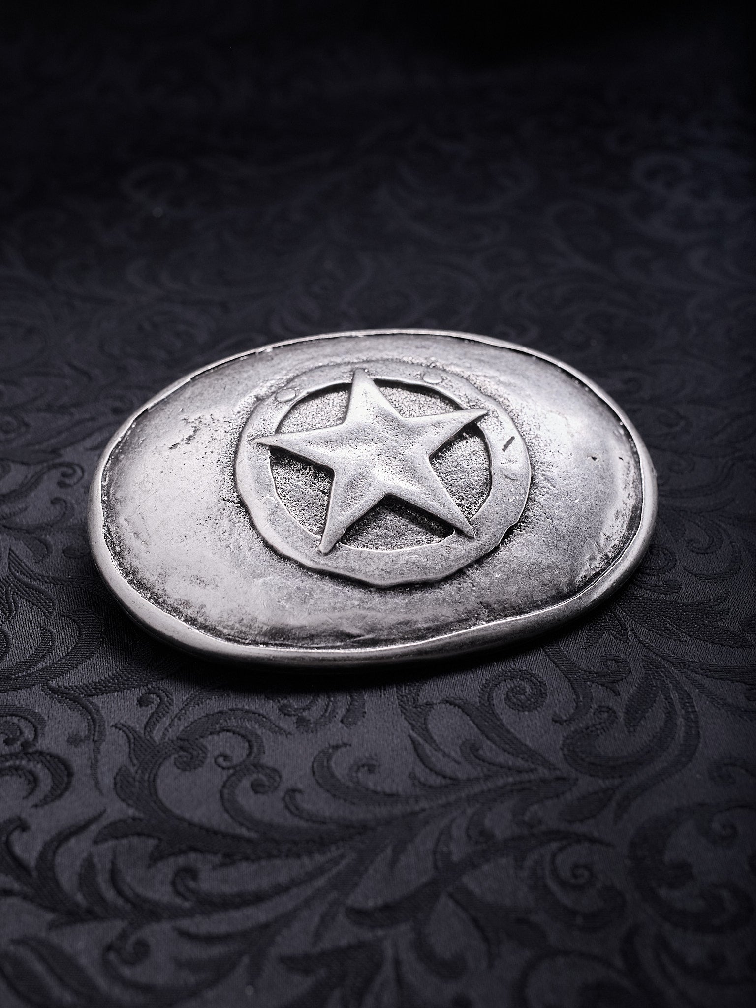 Detailed close-up of the raw grainy texture and oxidized silver-tone finish on the Frontier Star belt buckle