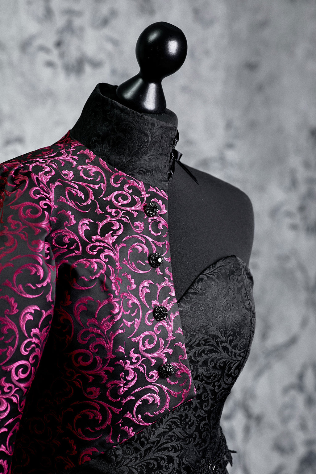 Close-up of handcrafted magenta fabric rose on black jacquard brocade with intricate baroque scroll embossed pattern