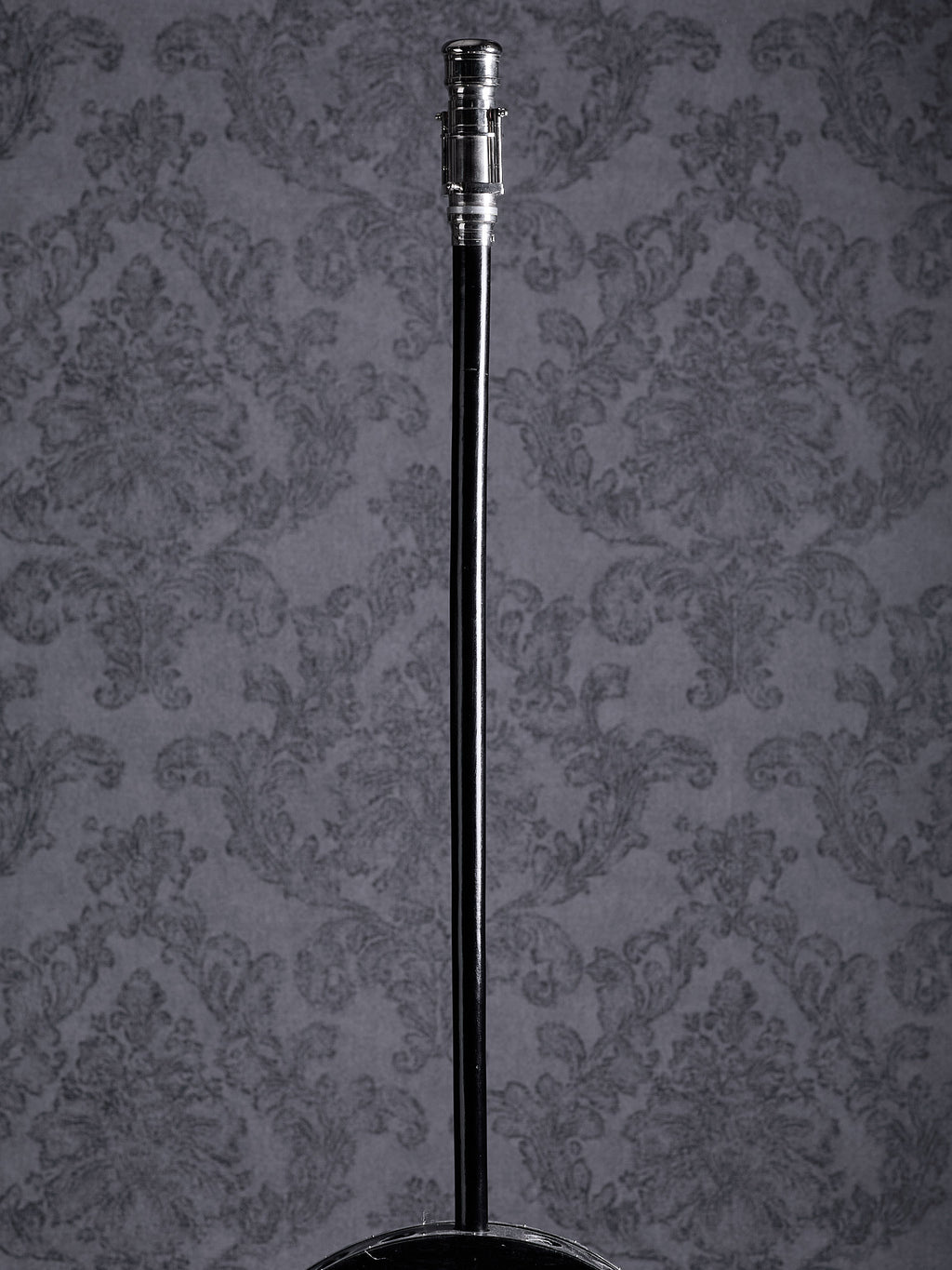 Full-length view of the Industrial Voyager walking cane with a silver handle and black wooden shaft on a grey patterned background