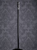 Full-length view of the Industrial Voyager walking cane with a silver handle and black wooden shaft on a grey patterned background