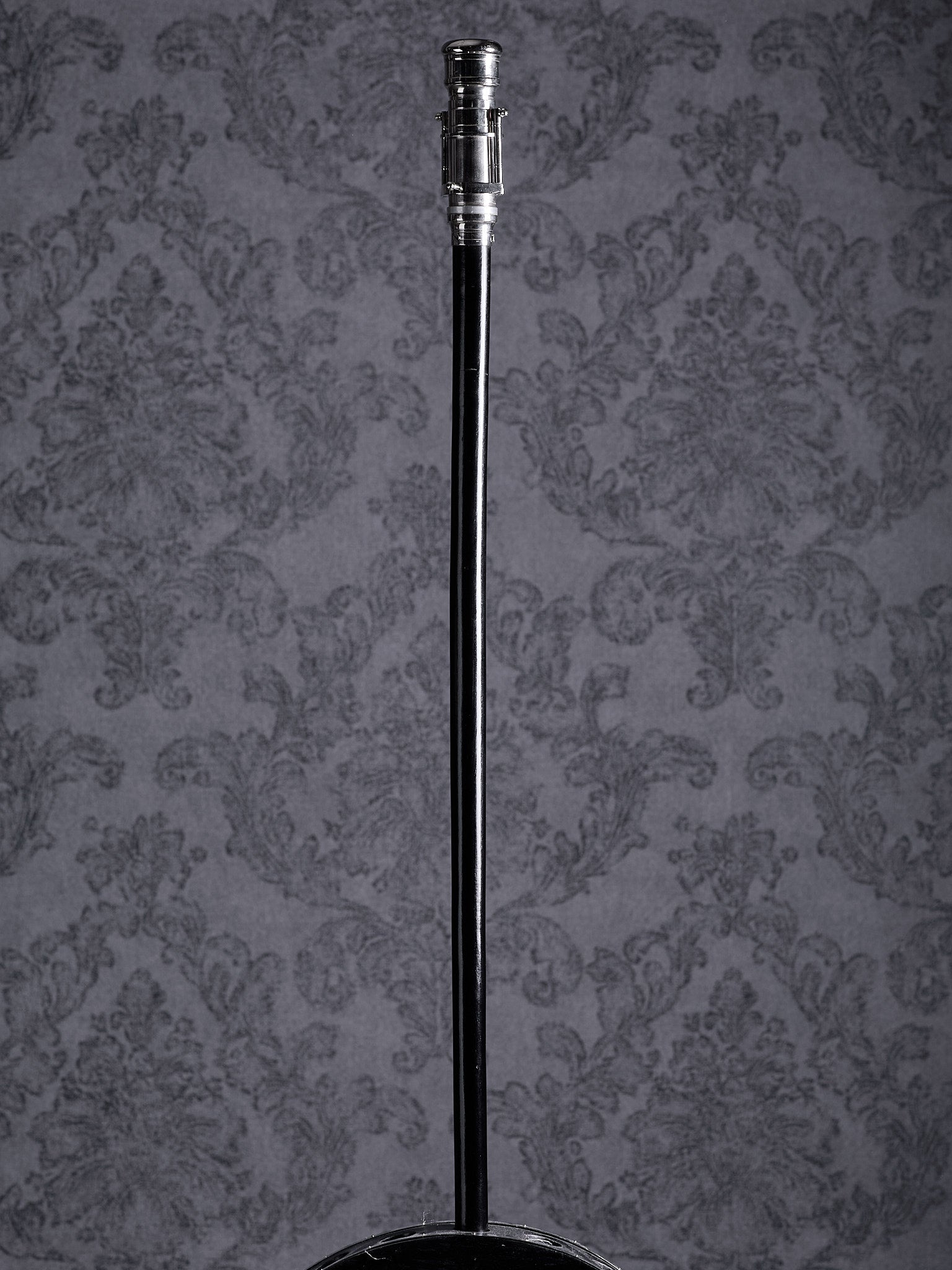 Full-length view of the Industrial Voyager walking cane with a silver handle and black wooden shaft on a grey patterned background