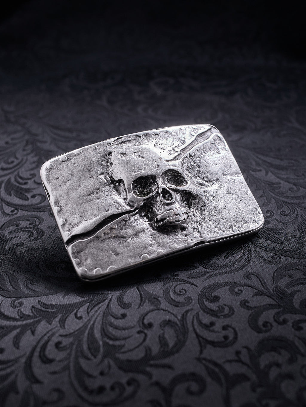 Detailed close-up of the coarse, grainy metal surface and skull engraving on the Memento Fracture buckle