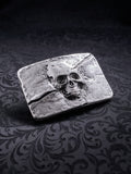 Detailed close-up of the coarse, grainy metal surface and skull engraving on the Memento Fracture buckle