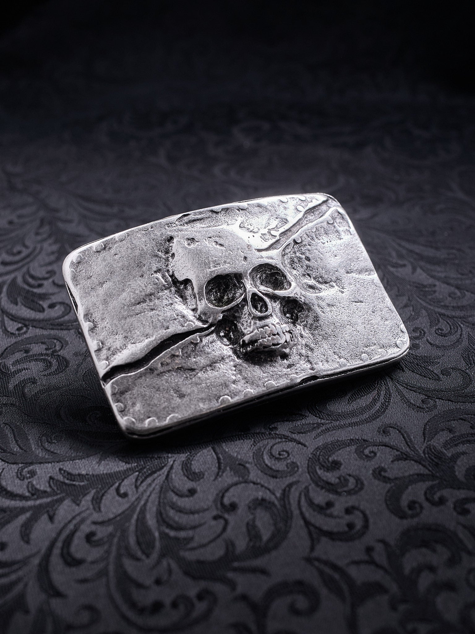 Detailed close-up of the coarse, grainy metal surface and skull engraving on the Memento Fracture buckle