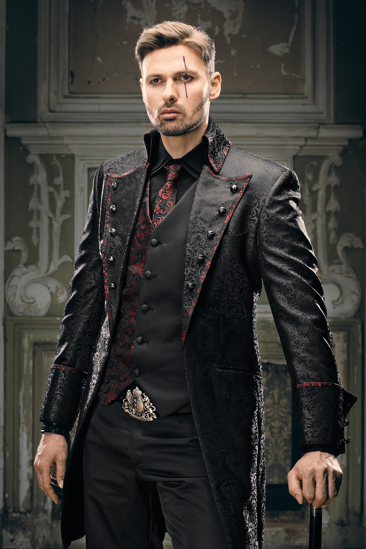 Men's black Victorian frock coat with red brocade lapel lining, skull buttons and ornate heraldic buckle, styled with black trousers and cane for gothic wedding