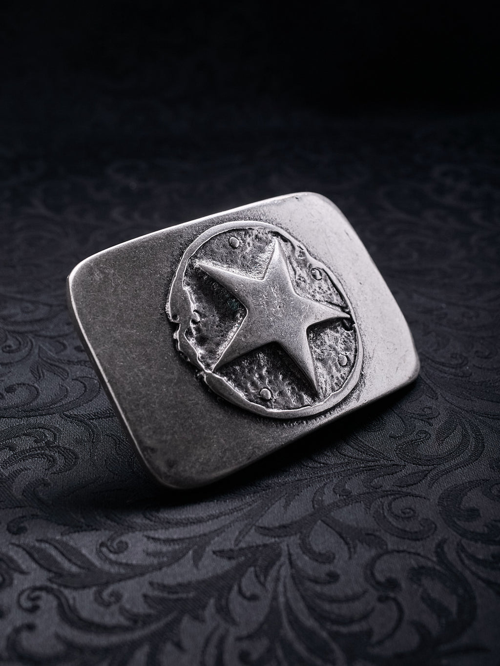 Detailed close-up of the rugged, grainy metal texture and oxidized silver finish on the Silent Star buckle