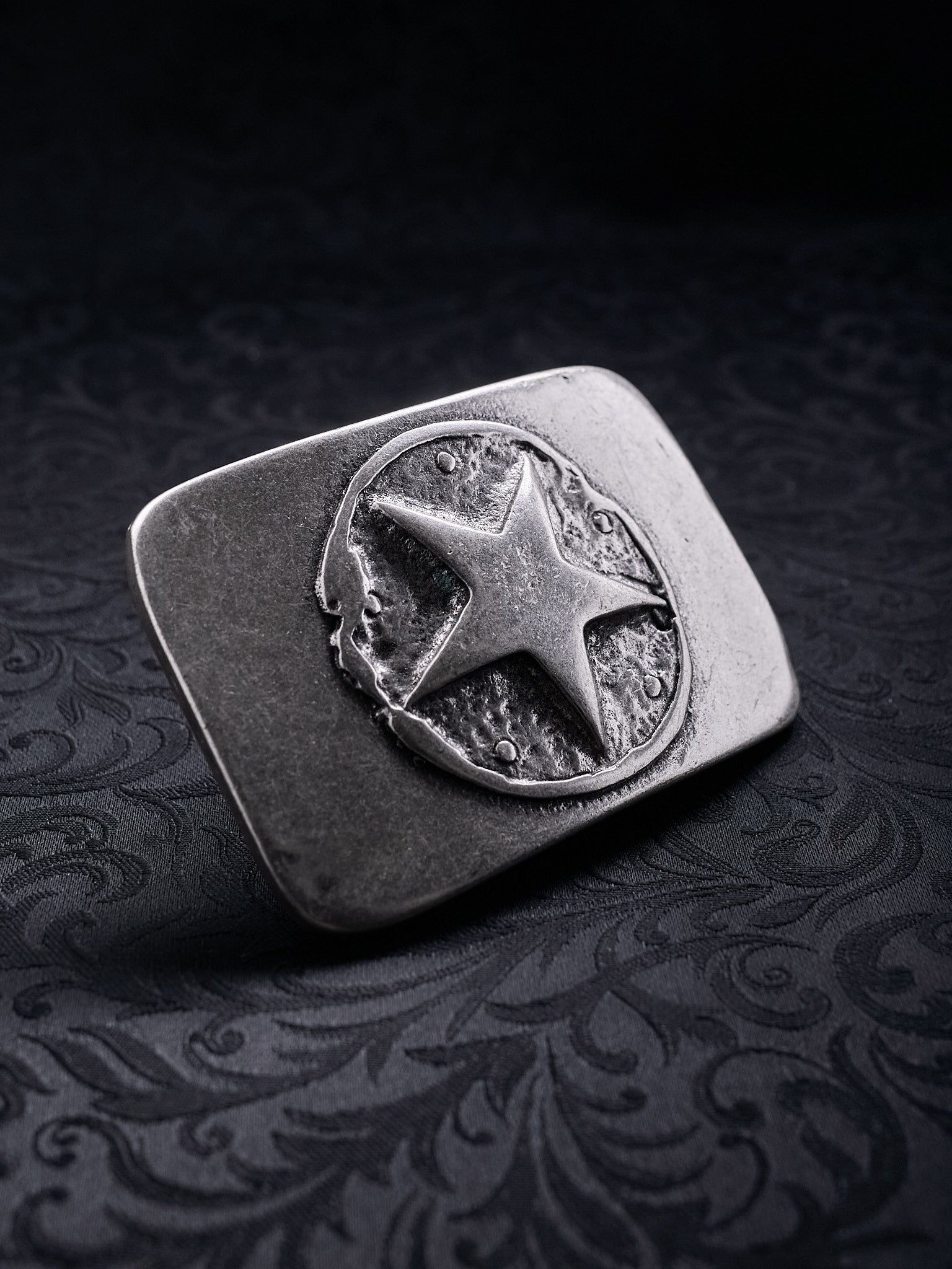 Detailed close-up of the rugged, grainy metal texture and oxidized silver finish on the Silent Star buckle