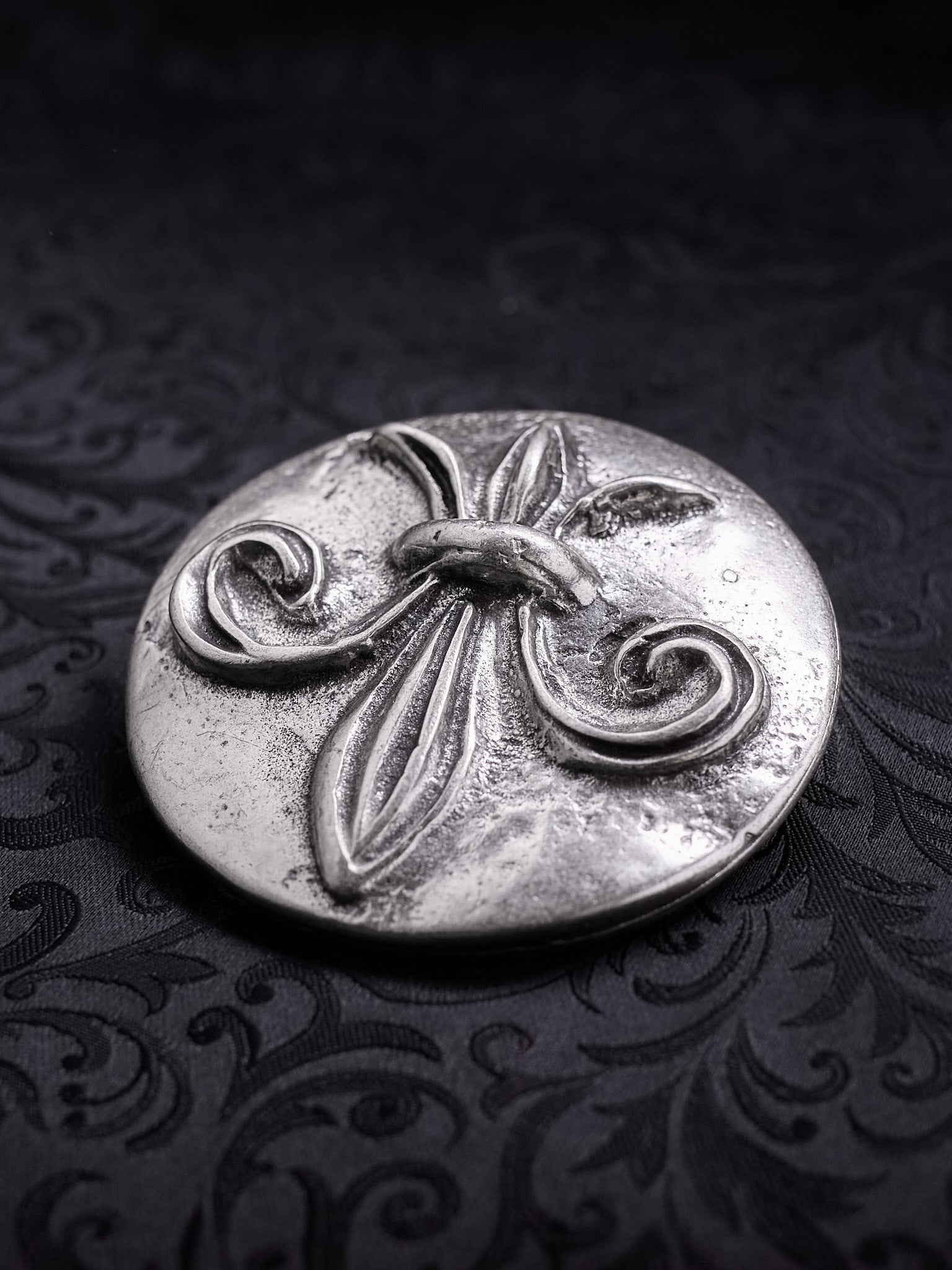 Round metal belt buckle named Sable Fleur with a central Fleur-de-lis relief on a dark background