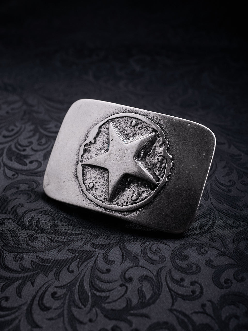 Rectangular metal belt buckle named Silent Star with a central star in a cratered circle on a black background