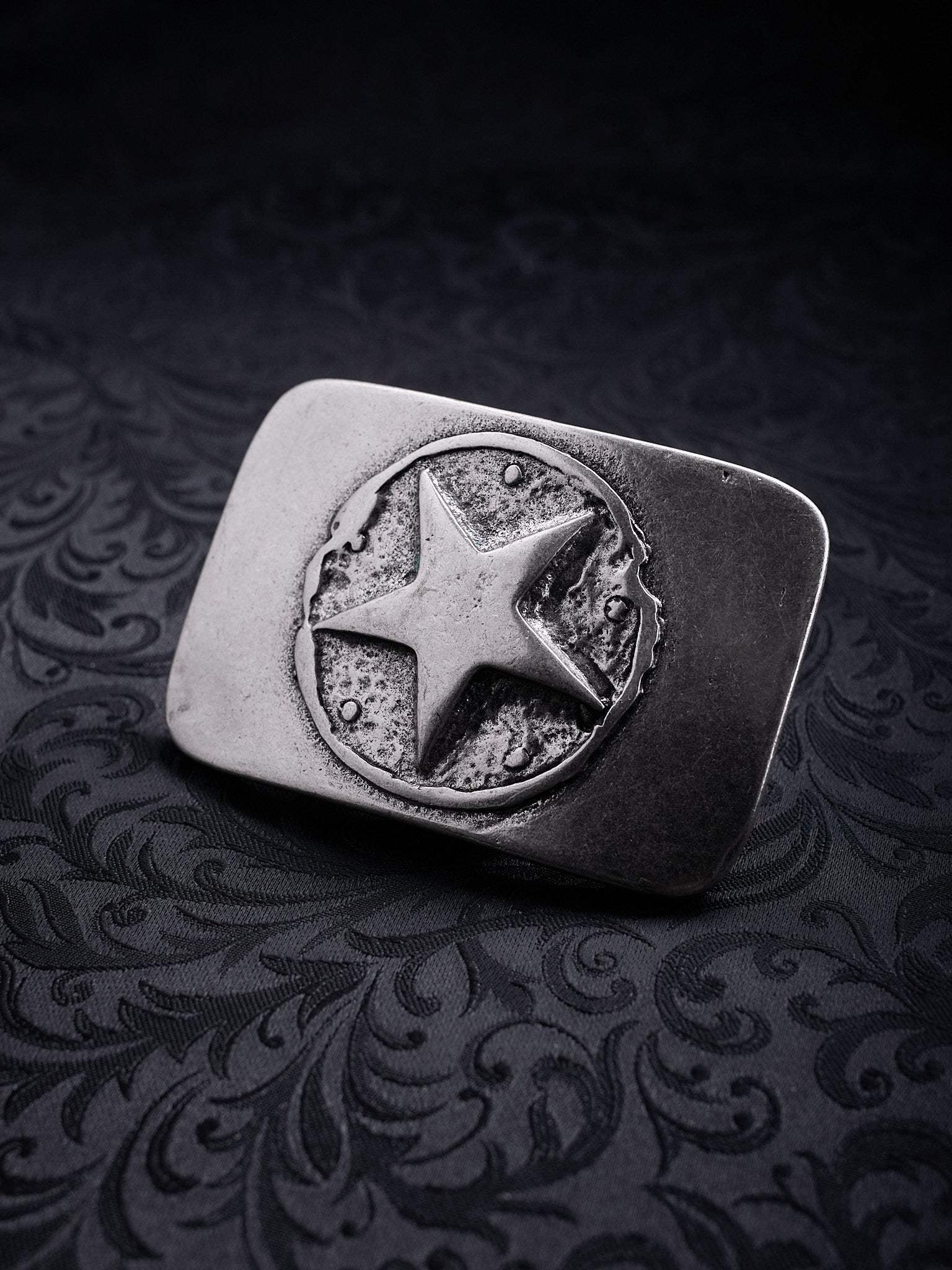Rectangular metal belt buckle named Silent Star with a central star in a cratered circle on a black background