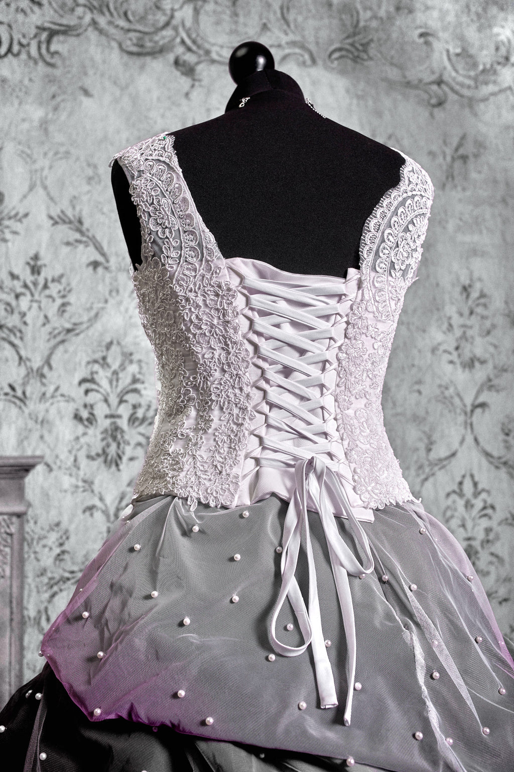 Back lace-up corset detail on white gothic wedding dress with satin ribbon threading through boned lace bodice, purple ombre tulle skirt visible below